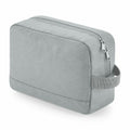 The BG277 by Bagbase is a light gray, rectangular toiletry bag featuring a zipper closure and a side handle. Its subtly textured fabric provides a modern, minimalist look, and the bag is slightly angled to highlight the zipper and handle details.