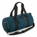 The Bagbase BG284 is a teal duffel bag with black straps, including a detachable shoulder strap. It boasts a cylindrical design with a top zipper closure and features a zippered front pocket for added convenience.