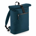 A Bagbase roll-top backpack in dark teal, featuring a black adjustable strap and a front zippered pocket, identified as product BG286, stands upright against a white background.