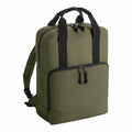 A Bagbase BG287 green backpack featuring black zippers and handles is showcased against a plain white background. The bag includes a front pocket and adjustable shoulder straps.