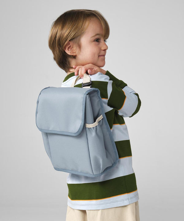 A young child with light brown hair, in a green and white striped shirt and beige shorts, stands sideways holding the Bagbase Kids' Adventure Cooler Bag over their shoulder against a plain grey background.