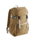 The Bags tan canvas rucksack features white and black buckles, a front zip pocket, side pockets, and adjustable shoulder straps, displayed on a white background.