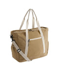 The Bags canvas tote is beige with white handles and an adjustable shoulder strap. It features a front zipped pocket, side pockets, and a zipped main compartment.