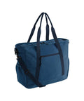 A Bags tote in blue fabric features two dark blue shoulder straps, a front zippered pocket, side pockets, and a detachable cross-body strap, displayed against a white background.