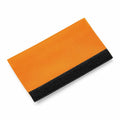 The Bagbase BG485 is displayed on a white background, featuring an orange and black fabric design. It sports a simple rectangular shape with a contrasting black edge at the bottom.