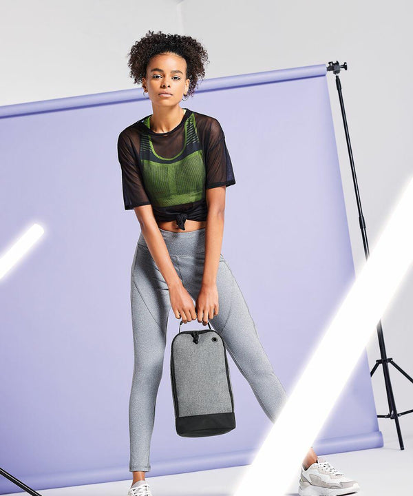 Person in athletic attire holds a gray Bagbase BG540 while standing against a light purple backdrop with studio lighting equipment visible.