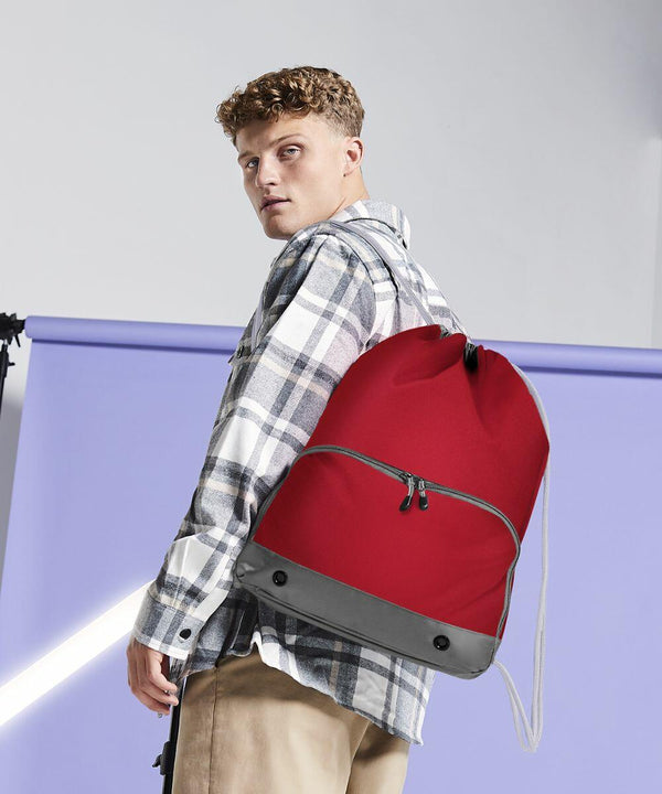 A person wearing a plaid shirt and khaki pants is carrying a red Bagbase BG542 backpack.
