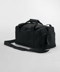 A black Bagbase BG560 with a rectangular shape, zippered main compartment, and front zippered pocket is shown. It features two handles with a padded grip and an adjustable shoulder strap. The bag is displayed against a plain white background.