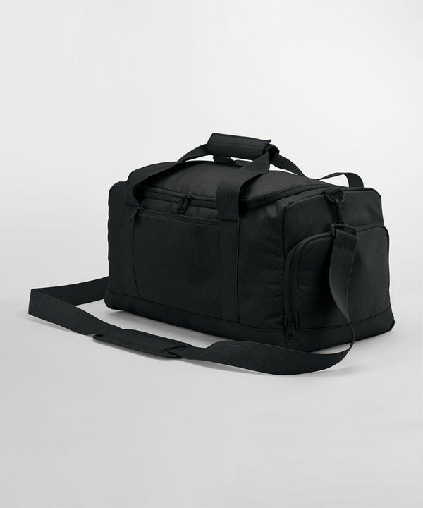 A black Bagbase BG560 with a rectangular shape, zippered main compartment, and front zippered pocket is shown. It features two handles with a padded grip and an adjustable shoulder strap. The bag is displayed against a plain white background.