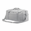 The Bagbase BG561 is a light gray duffel bag featuring a zippered front pocket, top handles, and a detachable shoulder strap. With its rectangular shape and additional side pockets, this bag is perfect for travel or gym use.