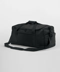 A large black Bagbase BG561 with a front zipper pocket, two handles, and a detachable shoulder strap is displayed on a plain white background. The bag appears to be made from a durable fabric material.