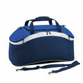 Introducing the Bagbase BG572, a stylish blue and white duffel bag featuring a durable handle and detachable shoulder strap. It boasts a spacious zippered main compartment along with convenient side pockets, all showcased against a plain white background.