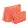 Displayed side by side are two coral-colored Bagbase BG751 zippered pouches of different sizes, each featuring elegant gold zippers.