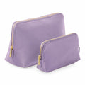 The BG751 by Bagbase features two lavender-colored zippered pouches with gold zippers, one larger and one smaller, arranged side by side. These pouches boast a simple, elegant design and a smooth texture.