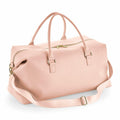 The Bagbase BG760 is a blush pink leather duffel bag that features gold hardware, double handles, and an adjustable shoulder strap. Its main compartment is secured with a zipper.