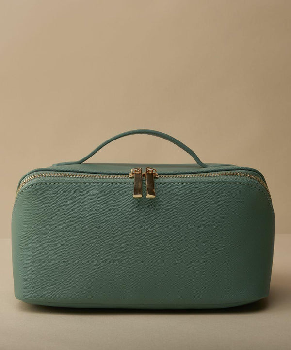A teal, rectangular travel toiletry bag with a textured surface is displayed against a beige background. The Bagbase BG762 features a handle on top and a gold zipper with two pulls in the center.