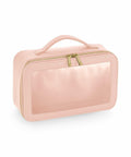 The Bagbase BG764 is a trapezoidal-shaped toiletry bag in pink, featuring a transparent front panel and a gold zipper. It also includes a small handle on top for easy carrying.