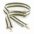 The BG765 by Bagbase features a beige adjustable strap adorned with black stripes and gold-tone metal clips at each end. The strap is elegantly displayed with a twist, highlighting its length and unique details.