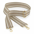 The Bagbase BG765 features a beige strap adorned with white stripes and gold hardware, including two swivel clips and an adjustable buckle. The strap is displayed neatly on a white background.