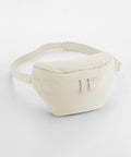 A minimalist beige fanny pack on a white background. The Bagbase BG875 has a smooth, rectangular shape with rounded edges, an adjustable strap, and a zippered main compartment. The material looks soft and slightly padded.