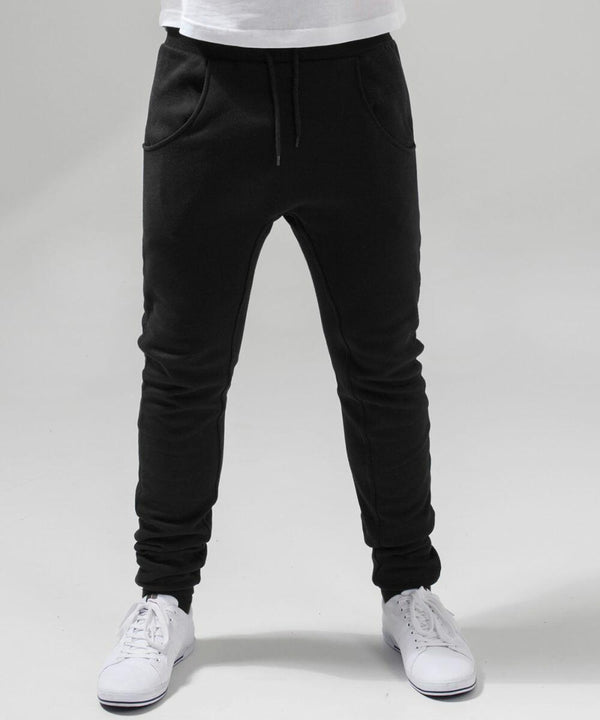 Person wearing Build Your Brand's BY013 jogger pants with an elastic waistband and drawstrings, paired with white sneakers. The background is plain white. The person's hands are in the pockets of the joggers, and the photo is cropped below the waist.