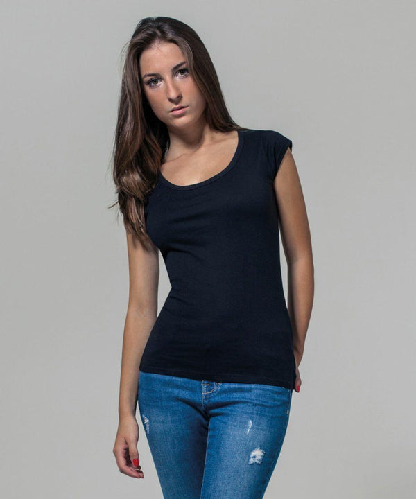 A person with long brown hair, wearing a black short-sleeved BY035 top from Build Your Brand and blue jeans, poses against a plain grey background. Their left hand rests casually on their hip while their right arm hangs by their side.