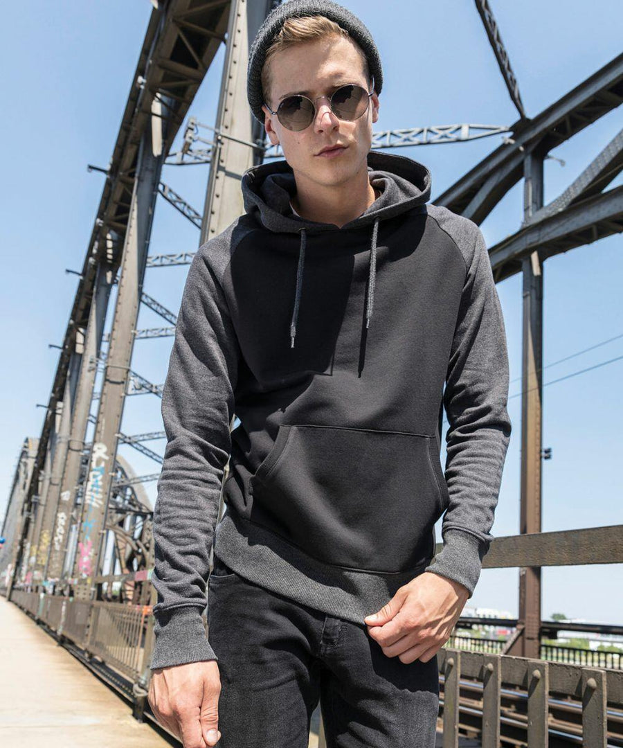 A person wearing BY077 by Build Your Brand, a dark hoodie, and a beanie stands on an industrial bridge during the day.