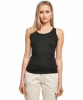 A woman with shoulder-length blonde hair is wearing a black sleeveless top and beige pants from the Build Your Brand BY089 collection, standing against a plain white background.