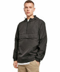 A person stands facing forward wearing a black hooded pullover jacket and beige pants against a plain white background. This jacket is the BY096 by Build Your Brand.