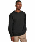 A man wearing a black Build Your Brand BY119 sweatshirt and beige cargo pants stands against a white background.
