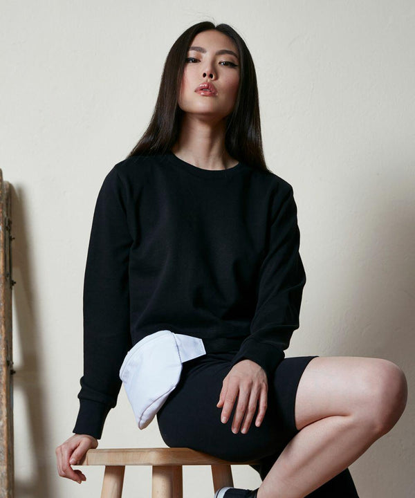 A person with long dark hair sits on a stool, wearing a black sweatshirt and shorts, with a white BY131 accessory from Build Your Brand draped over their leg.