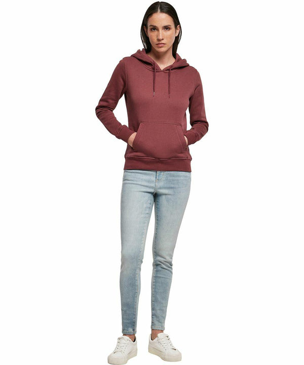A person stands facing forward, wearing a maroon BY139 hoodie from Build Your Brand, light blue jeans, and white sneakers.