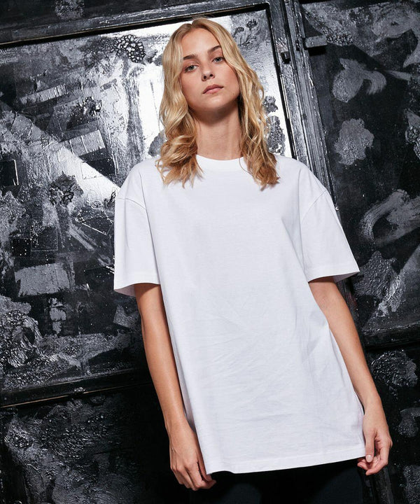 A person with long blonde hair wearing a plain white Build Your Brand BY149 t-shirt stands in front of a dark, textured background.