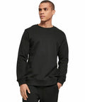 A person wearing a plain black BY173 sweater by Build Your Brand and black pants, standing against a white background.
