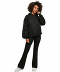 Person wearing a black BY183 hoodie and black pants from Build Your Brand stands with one hand by their side and the other touching their face, against a white background.