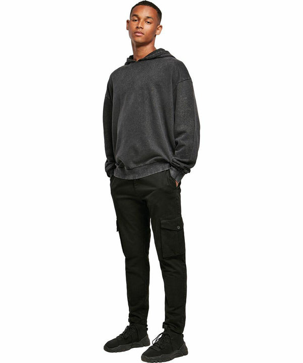 A person stands with hands in pockets, wearing a dark gray hoodie, black cargo pants, and black Build Your Brand BY191 sneakers, against a plain white backdrop.