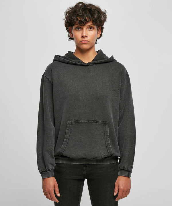 Person with short curly hair wearing a dark gray Build Your Brand BY194 hoodie with a front pocket, standing against a plain background.