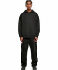 A person stands facing forward, wearing a BY199 hoodie by Build Your Brand, black pants, and black shoes, with their hands by their sides.
