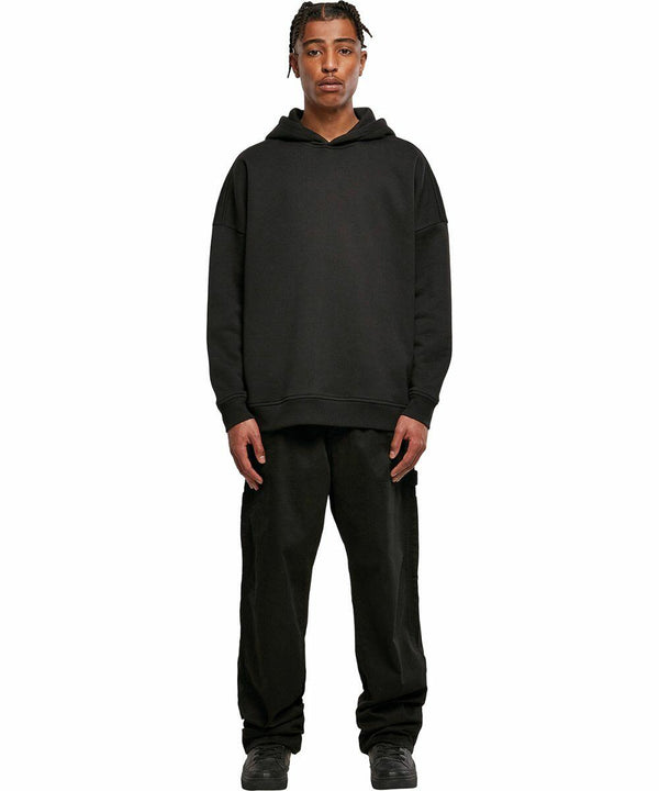 A person stands facing forward, wearing a BY199 hoodie by Build Your Brand, black pants, and black shoes, with their hands by their sides.