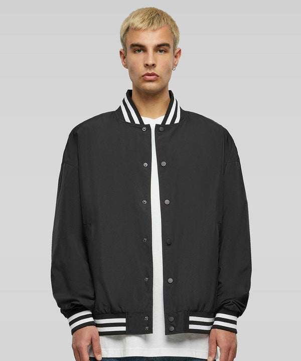 A person with short blond hair wearing a black BY259 varsity jacket by Build Your Brand over a white shirt stands against a plain background.