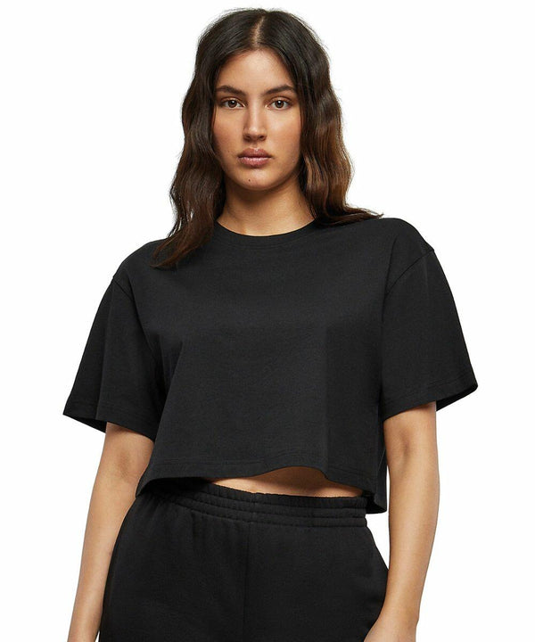 Person wearing a black cropped T-shirt and black pants, specifically the BY264 from Build Your Brand, standing in front of a plain white background.