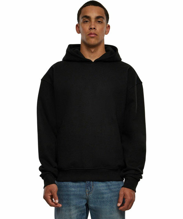 A person wearing a Build Your Brand BY268 plain black hoodie and blue jeans standing against a white background.