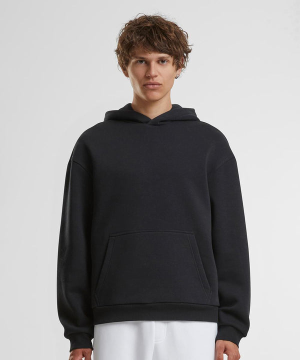 A person with short, curly brown hair wears the Build Your Brand Fluffy hoodie in black and white trousers, standing against a plain white background and facing the camera.