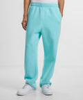 A person models the lower half of Build Your Brand’s Fluffy track bottoms in light blue with white trainers, hands in pockets, standing against a plain white background.