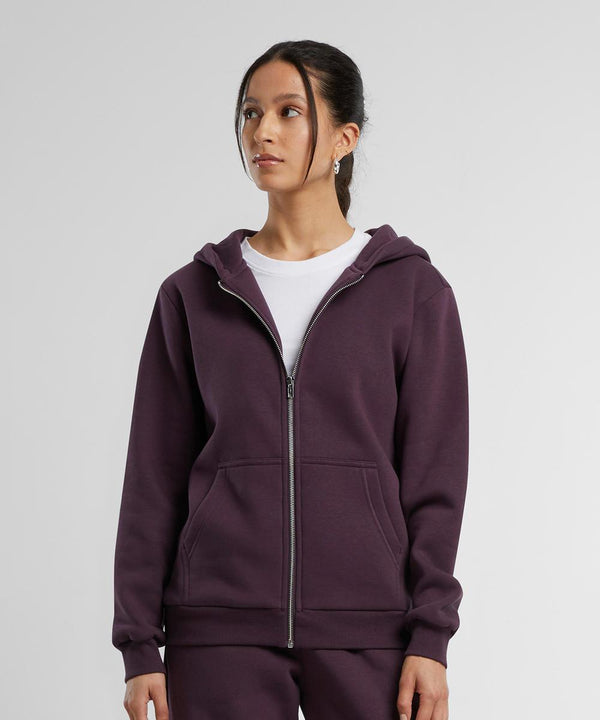 A woman with dark hair pulled back wears the Build Your Brand Women’s fluffy zip hoodie in dark purple over a white T-shirt, standing against a plain background and looking slightly to the side with a neutral expression.