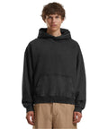 A person with short, curly hair models the Build Your Brand Vintage heavy hoodie in black with beige trousers, standing against a plain white background.