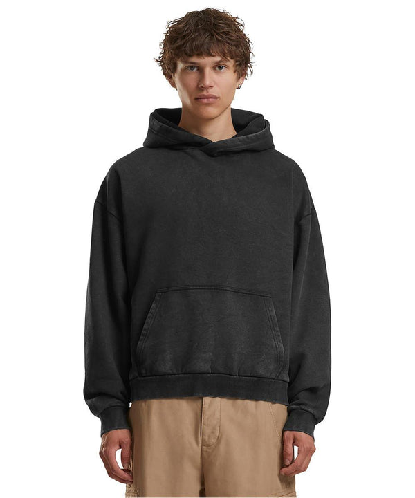 A person with short, curly hair models the Build Your Brand Vintage heavy hoodie in black with beige trousers, standing against a plain white background.