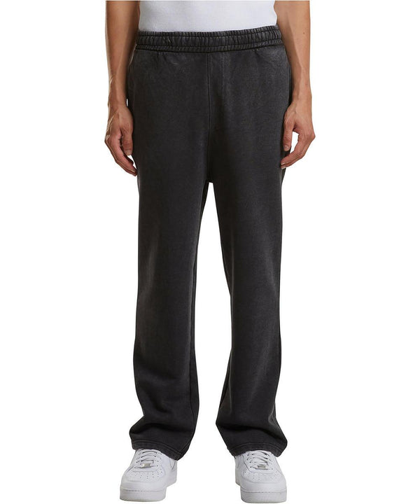 A person is shown from the waist down, wearing Build Your Brand Vintage heavy trackpants in black with hands in pockets, paired with a white shirt and white trainers, standing against a plain white background.