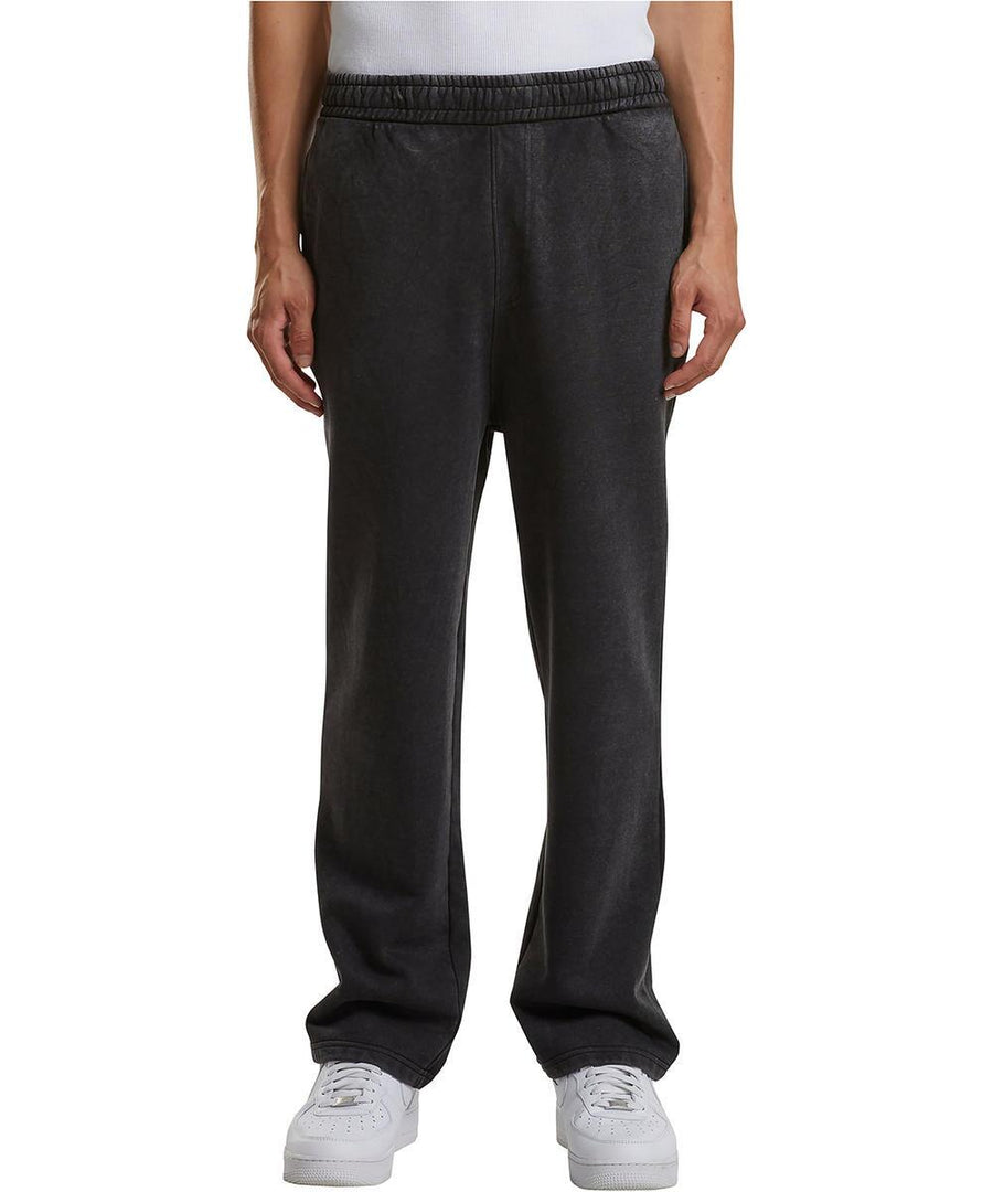 A person is shown from the waist down, wearing Build Your Brand Vintage heavy trackpants in black with hands in pockets, paired with a white shirt and white trainers, standing against a plain white background.