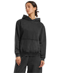 A woman in the Build Your Brand Women's vintage heavy hoodie, a loose-fitting dark grey sweatshirt with a front pocket and hood, stands against a white background, gazing slightly to the side.